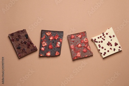 Different chocolate bars with freeze dried fruits on beige background, flat lay