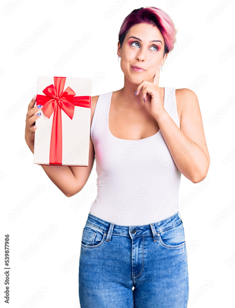 Young beautiful woman with pink hair holding gift serious face thinking about question with hand on chin, thoughtful about confusing idea Young beautiful woman with pink hair holding gift serious face thinking about question with hand on chin, thoughtful about confusing idea