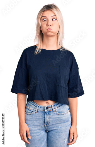 Young beautiful blonde woman wearing casual t-shirt puffing cheeks with funny face. mouth inflated with air, crazy expression. photo