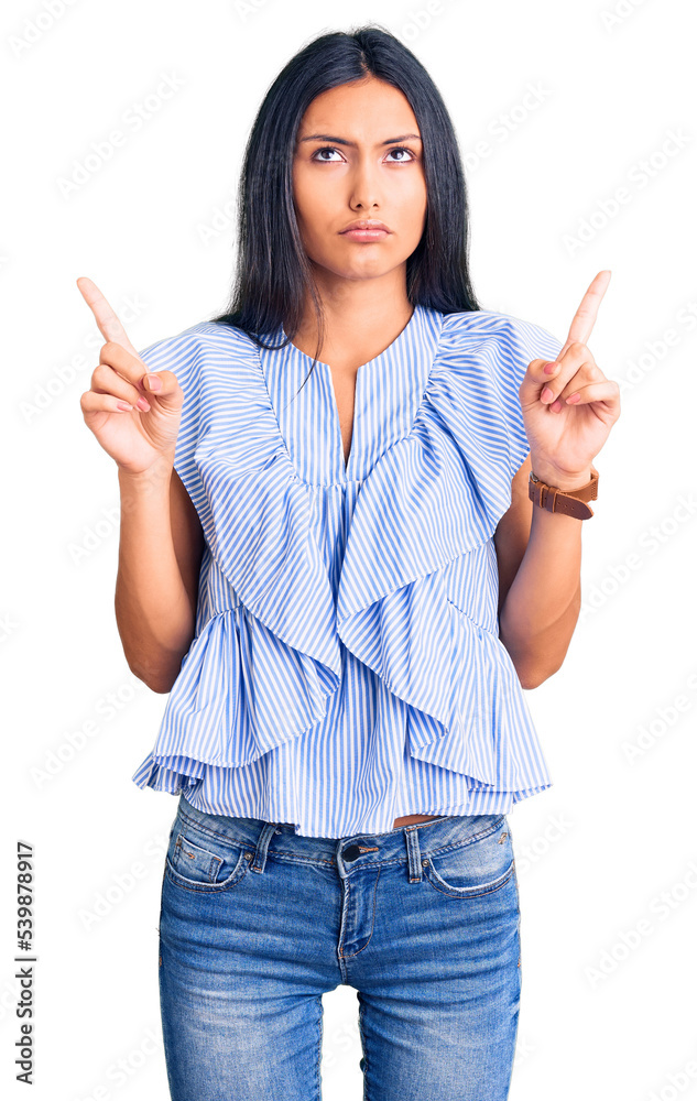 Young beautiful latin girl wearing casual clothes pointing up looking sad and upset, indicating direction with fingers, unhappy and depressed. Young beautiful latin girl wearing casual clothes pointing up looking sad and upset, indicating direction with fingers, unhappy and depressed.