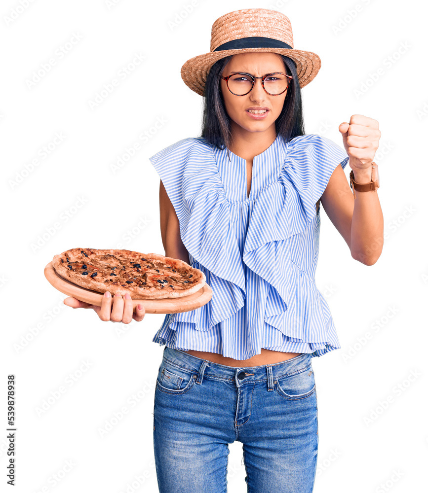 Young beautiful latin girl wearing summer hat and glasses holding pizza annoyed and frustrated shouting with anger, yelling crazy with anger and hand raised Young beautiful latin girl wearing summer hat and glasses holding pizza annoyed and frustrated shouting with anger, yelling crazy with anger and hand raised