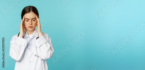 Image of woman doctor, medical personel grimacing from discomfort, having headache, migraine, feeling deezy, standing over torquoise background