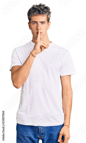 Young handsome man wearing casual white tshirt asking to be quiet with finger on lips. silence and secret concept.