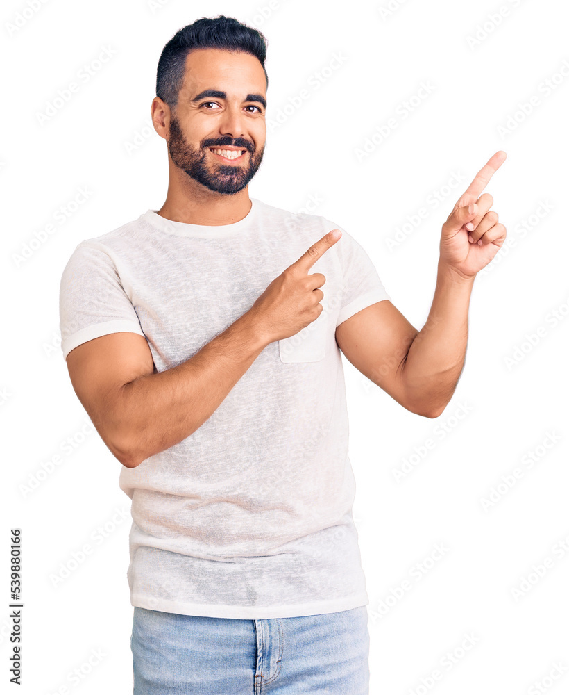 Young hispanic man wearing casual clothes smiling and looking at the camera pointing with two hands and fingers to the side.