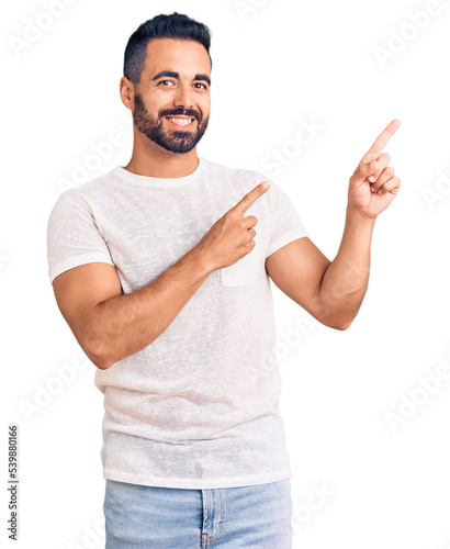 Fotografie, Tablou Young hispanic man wearing casual clothes smiling and looking at the camera pointing with two hands and fingers to the side