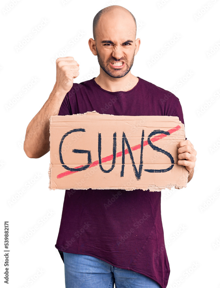 Young handsome man holding prohibited guns banner annoyed and frustrated shouting with anger, yelling crazy with anger and hand raised Young handsome man holding prohibited guns banner annoyed and frustrated shouting with anger, yelling crazy with anger and hand raised