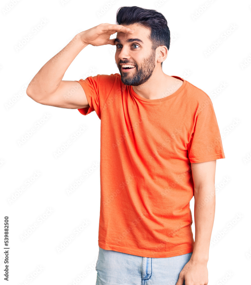 Young handsome man with beard wearing casual t-shirt very happy and smiling looking far away with hand over head. searching concept. Young handsome man with beard wearing casual t-shirt very happy and smiling looking far away with hand over head. searching concept.