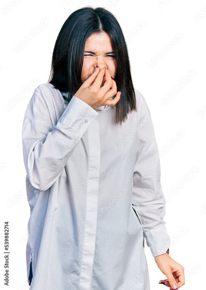 Young brunette woman with blue eyes wearing oversize white shirt smelling something stinky and disgusting, intolerable smell, holding breath with fingers on nose. bad smell Young brunette woman with blue eyes wearing oversize white shirt smelling something stinky and disgusting, intolerable smell, holding breath with fingers on nose. bad smell