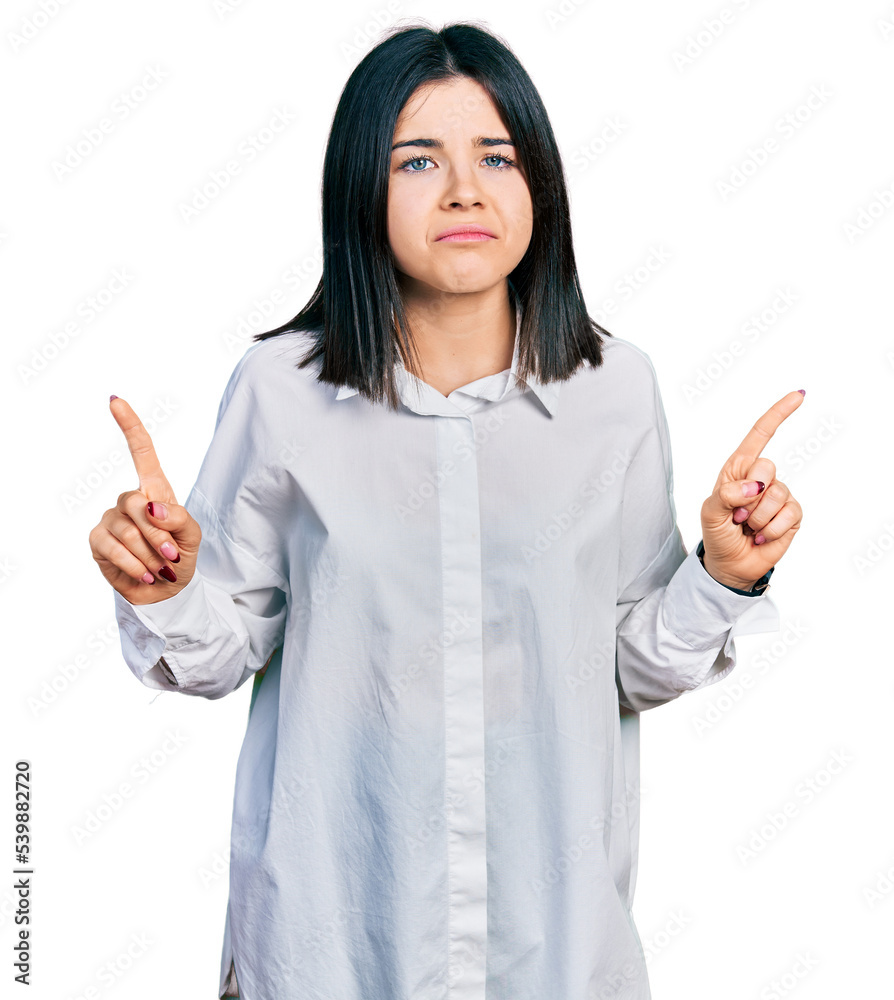Young brunette woman with blue eyes wearing oversize white shirt pointing up looking sad and upset, indicating direction with fingers, unhappy and depressed. Young brunette woman with blue eyes wearing oversize white shirt pointing up looking sad and upset, indicating direction with fingers, unhappy and depressed.