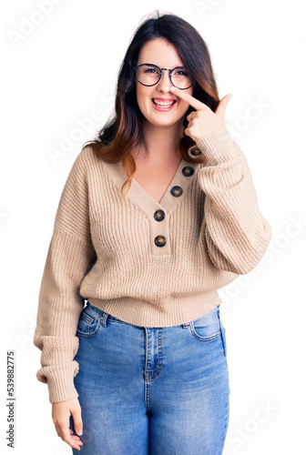 Beautiful young brunette woman wearing casual clothes and glasses pointing with hand finger to face and nose, smiling cheerful. beauty concept