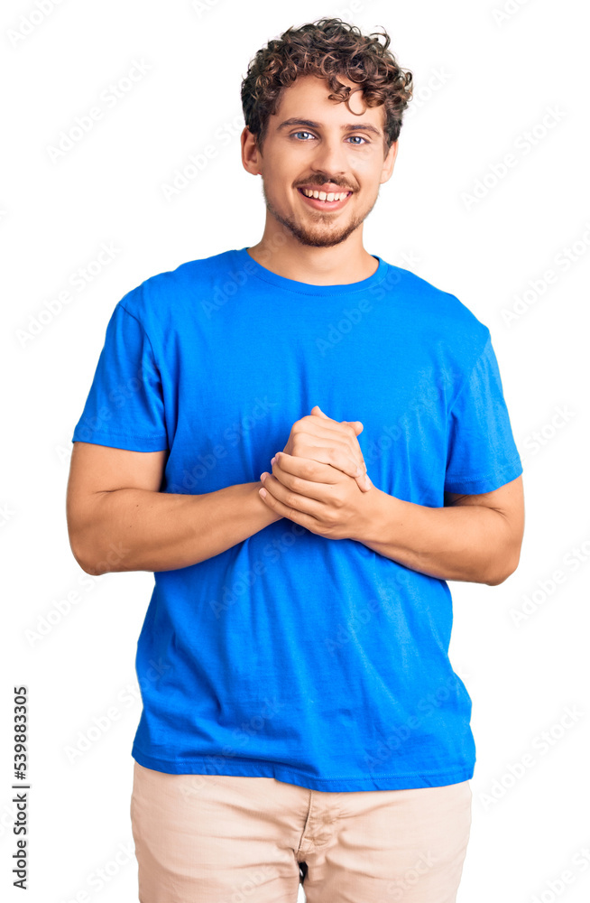 Young handsome man with curly hair wearing casual clothes with hands together and crossed fingers smiling relaxed and cheerful. success and optimistic