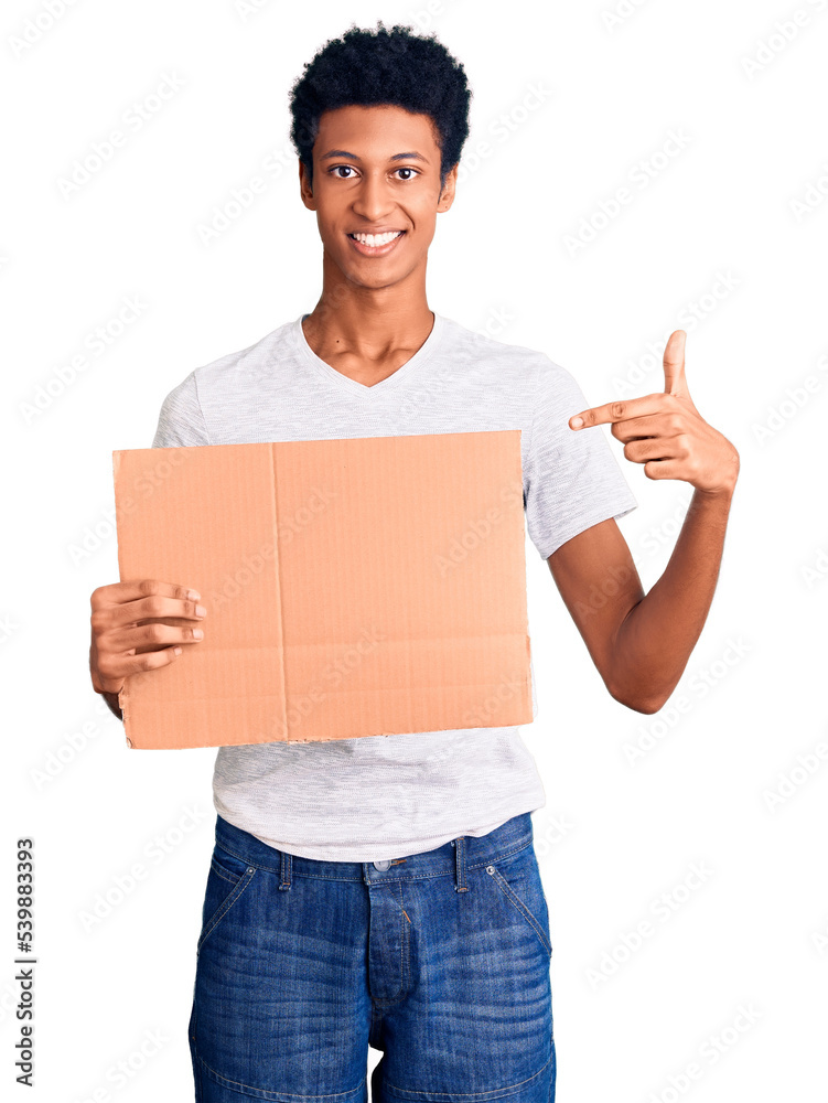 Young african american man holding banner cardboard smiling happy pointing with hand and finger Young african american man holding banner cardboard smiling happy pointing with hand and finger