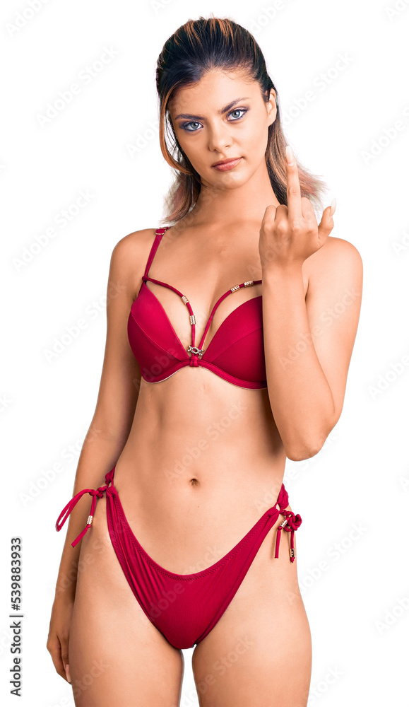 Young beautiful woman wearing bikini showing middle finger, impolite and rude fuck off expression Young beautiful woman wearing bikini showing middle finger, impolite and rude fuck off expression