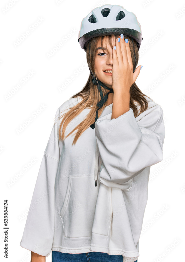 Teenager caucasian girl wearing bike helmet covering one eye with hand, confident smile on face and surprise emotion. Teenager caucasian girl wearing bike helmet covering one eye with hand, confident smile on face and surprise emotion.