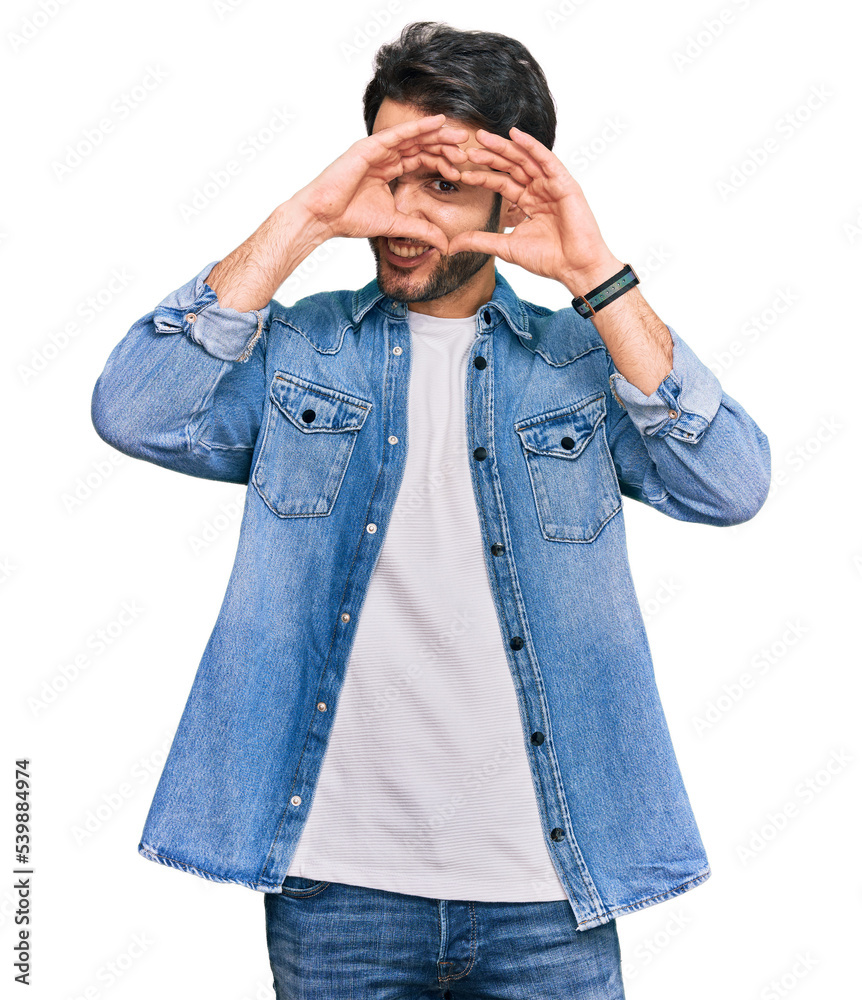 Young hispanic man wearing casual clothes doing heart shape with hand and fingers smiling looking through sign Young hispanic man wearing casual clothes doing heart shape with hand and fingers smiling looking through sign