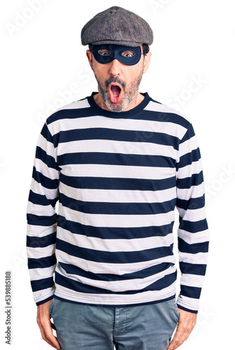 Middle age handsome man wearing burglar mask afraid and shocked with surprise expression, fear and excited face. © Krakenimages.com