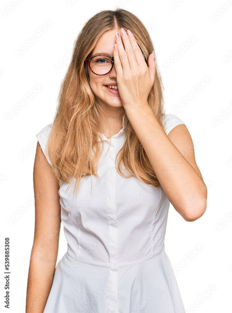 Beautiful young caucasian girl wearing casual clothes and glasses covering one eye with hand, confident smile on face and surprise emotion. Beautiful young caucasian girl wearing casual clothes and glasses covering one eye with hand, confident smile on face and surprise emotion.