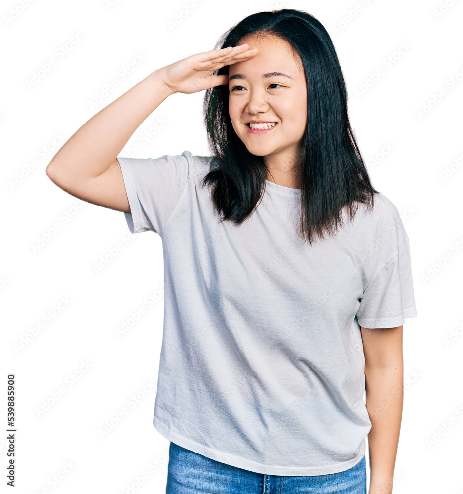 Young chinese woman wearing casual white t shirt very happy and smiling looking far away with hand over head. searching concept. Young chinese woman wearing casual white t shirt very happy and smiling looking far away with hand over head. searching concept.