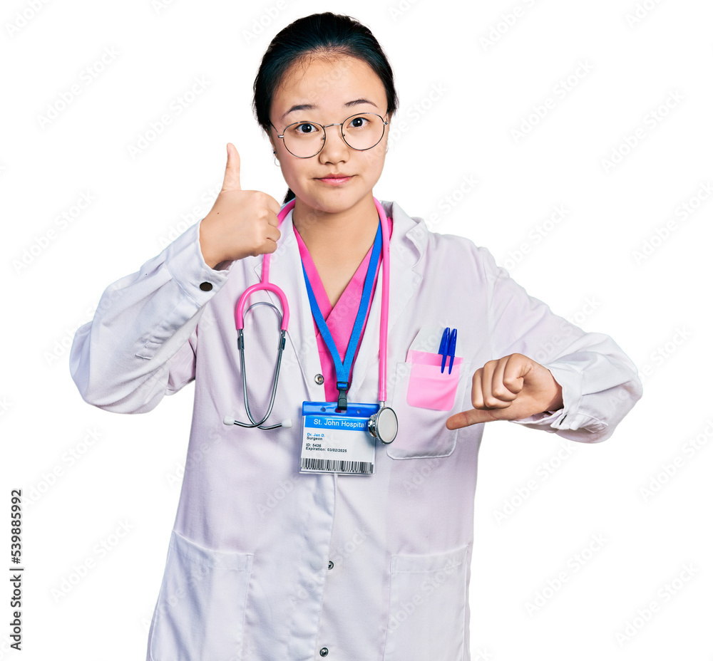 Young chinese woman wearing doctor uniform and stethoscope doing thumbs up and down, disagreement and agreement expression. crazy conflict Young chinese woman wearing doctor uniform and stethoscope doing thumbs up and down, disagreement and agreement expression. crazy conflict