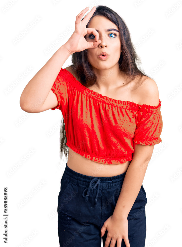 Brunette teenager girl wearing casual clothes doing ok gesture shocked with surprised face, eye looking through fingers. unbelieving expression.