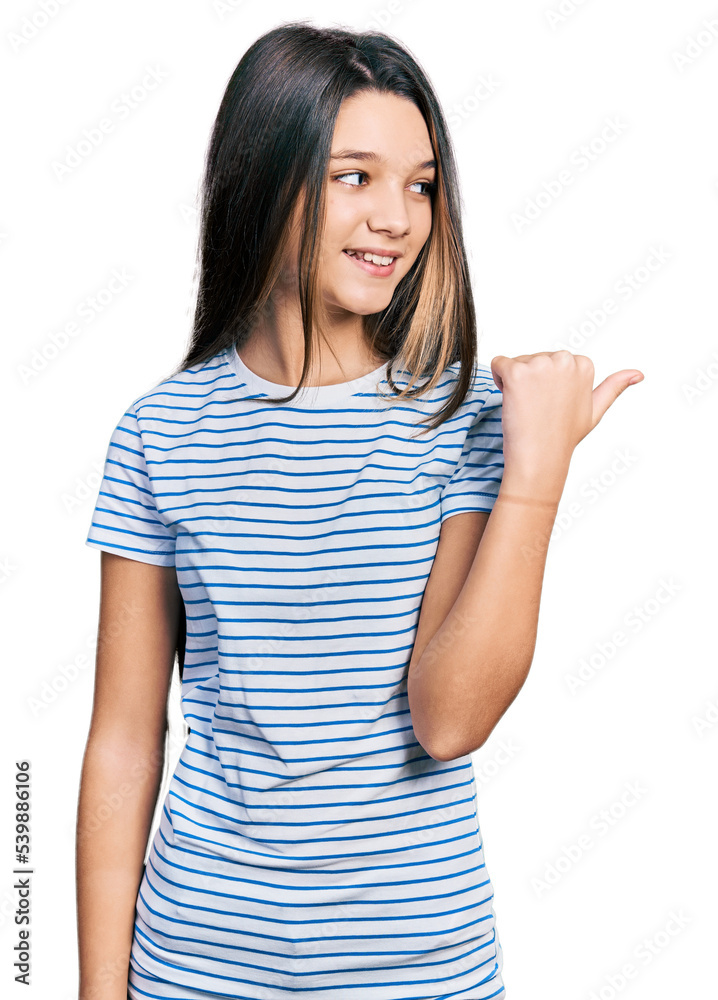 Young brunette girl with long hair wearing casual striped t shirt pointing thumb up to the side smiling happy with open mouth Young brunette girl with long hair wearing casual striped t shirt pointing thumb up to the side smiling happy with open mouth
