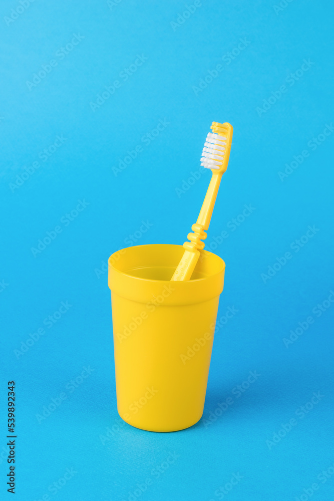 A yellow glass with a yellow toothbrush on a light blue background. A yellow glass with a yellow toothbrush on a light blue background.