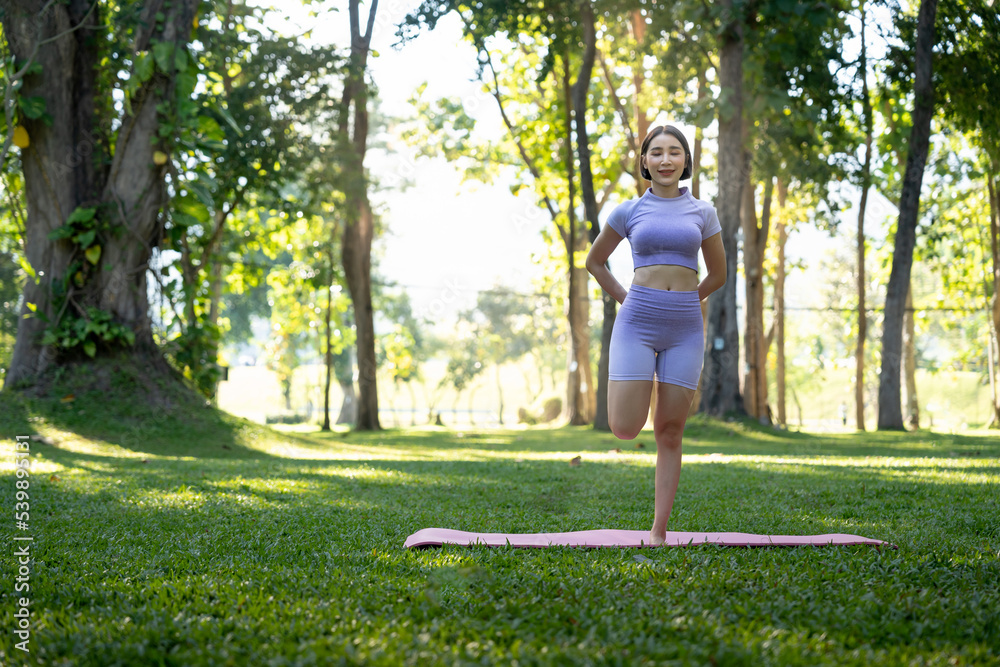 Attractive young Asian woman practice yoga, exercise in the park, standing one leg on a yoga mat, showing balance posture. Wellbeing lifestyle and activity concept