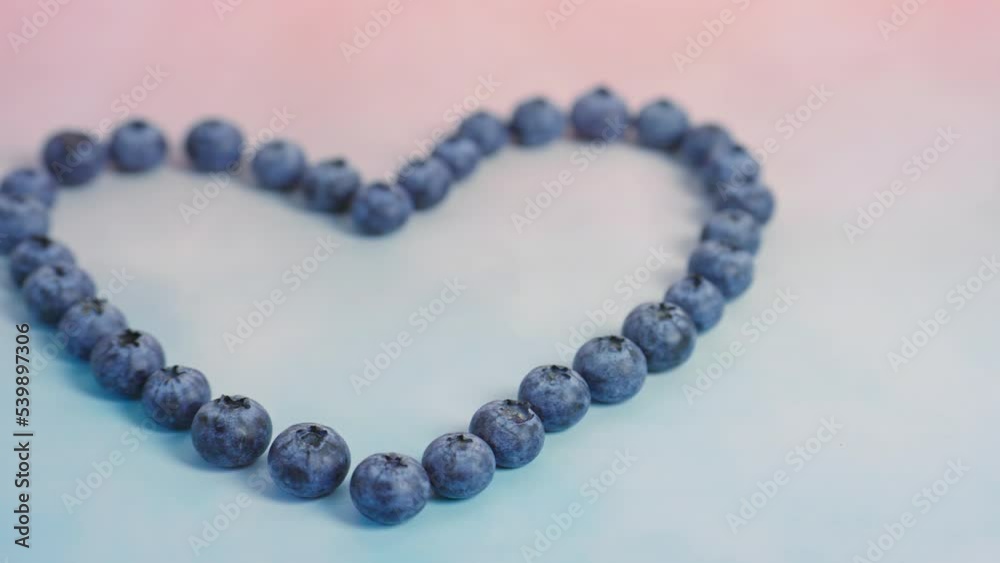 4k shots of healthy fresh fruit blueberries arranged in a heart shape and a pink and blue background