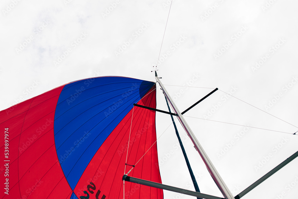 The red and blue gennaker of a sailing yacht catches the wind in an open state. Front view.