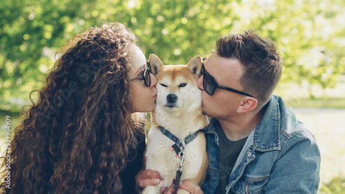 Loving owners of beautiful dog shiba inu are kissing the animal and petting it on the head while resting in the park together. Love, pets, people and healthy lifestyle concept. photo