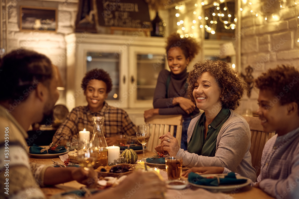 Happy mature black woman talking to her family during Thanksgiving meal at dining table.