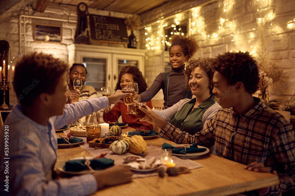 Happy black multigeneration family toasting while celebrating Thanksgiving at dining table.