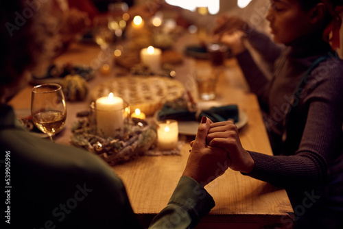 Close up of black family holding hands while saying grace during Thanksgiving meal.