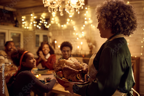 Happy black woman bringing Thanksgiving turkey to dining table during family lunch.