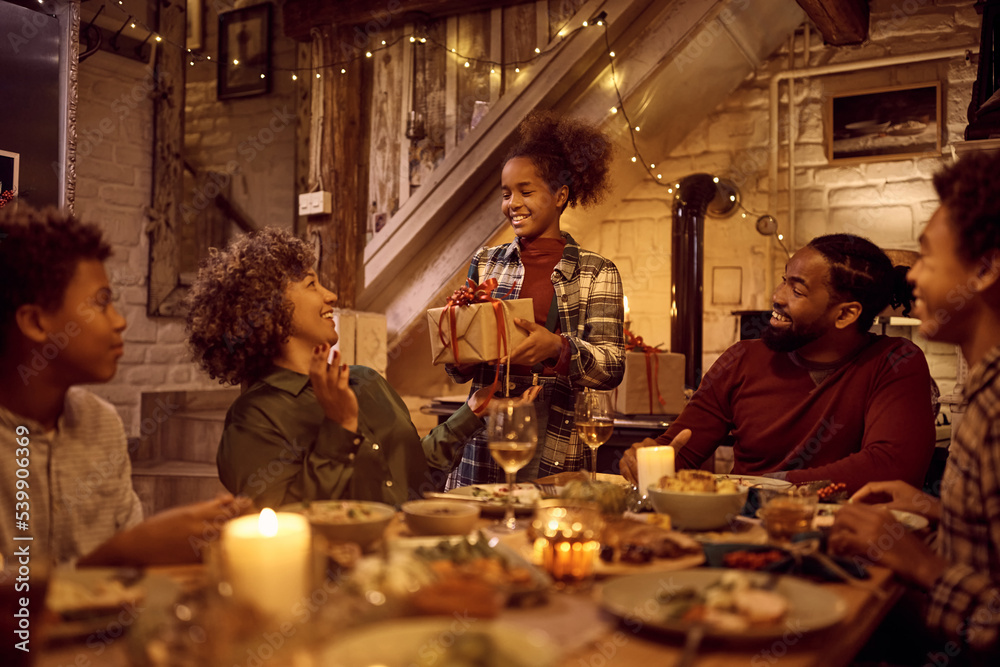Happy black woman receiving gift bx from her granddaughter while having Thanksgiving dinner at dining table. Happy black woman receiving gift bx from her granddaughter while having Thanksgiving dinner at dining table.