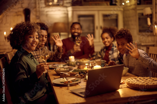 Happy black extended family making video call over laptop during Thanksgiving dinner at dining table.