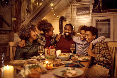Happy multigeneration black family embracing during Thanksgiving meal at dining table.