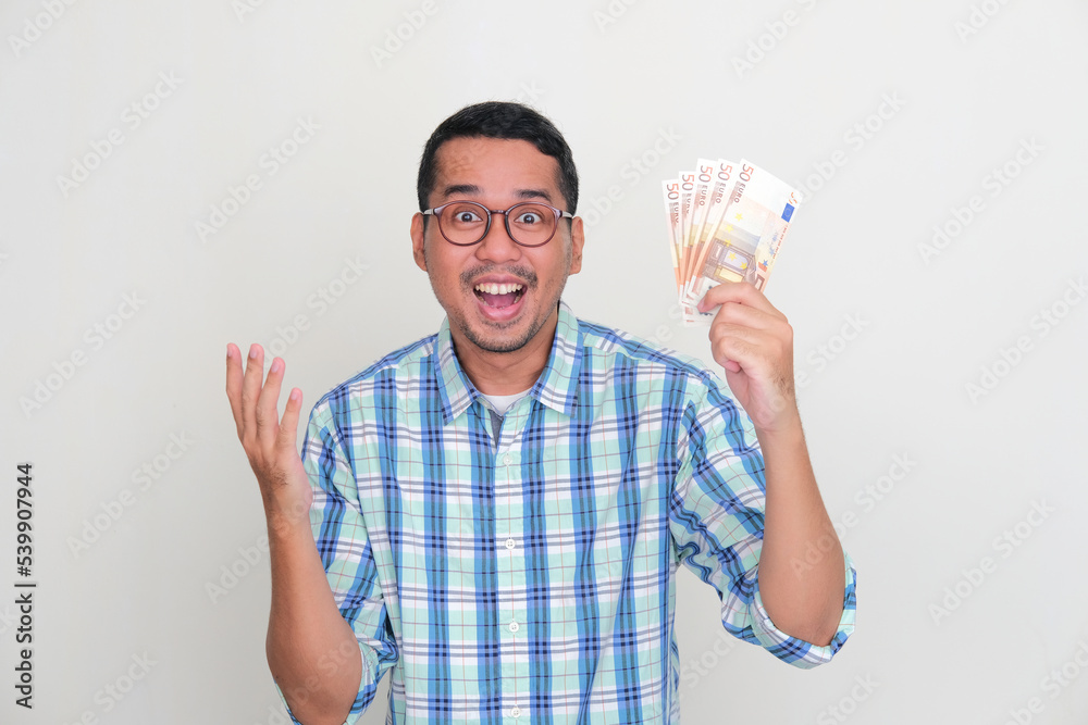 Asian man showing happy face expression while holding Euro currency Asian man showing happy face expression while holding Euro currency