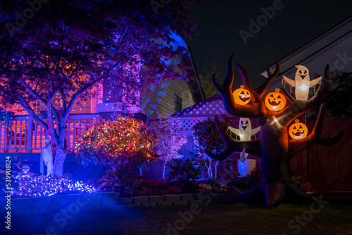 Night Halloween house outdoor decorations with glowing inflatable pumpkins and ghosts purple lights and orange garlands