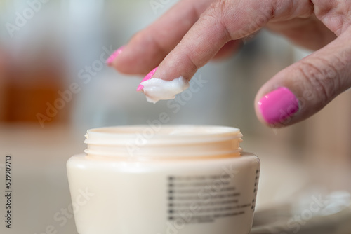 Senior woman s hand picking cream with her finger for personal skin care.