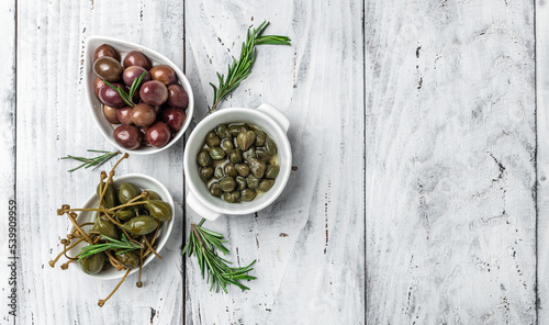 Caper berries and olives on white plate with fresh basil leaves on a gray background. Mediterranean snack assortment. banner, menu, recipe place for text, top view