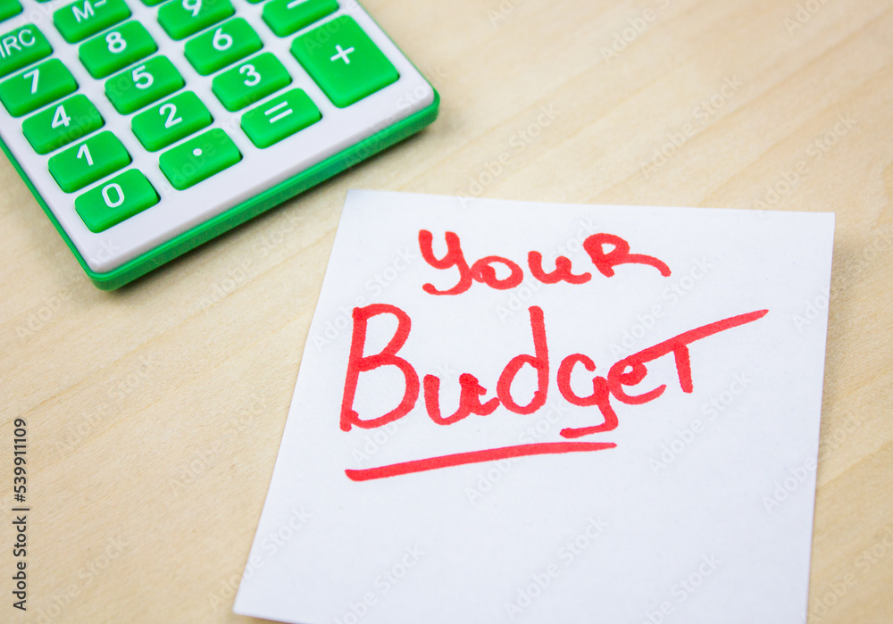 YOUR BUDGET text on sheet by red marker next to calculator on chalkboard YOUR BUDGET text on sheet by red marker next to calculator on chalkboard
