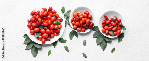 Plates with fresh rose hip berries and leaves on white background