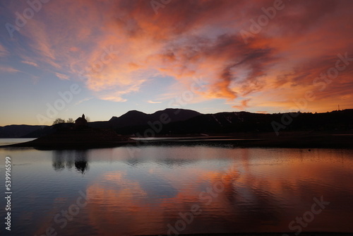 Fototapeta Naklejka Na Ścianę i Meble -  colorful sunset with mirror reflection above the island of the Bay St Michel in Serre Ponçon lake in the Southern Alps, France 