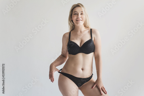 Young chubby woman with fat folds in black lingerie rear view on a gray background. The concept of body positivity and self acceptance. Sensual hot woman with forms in underwear