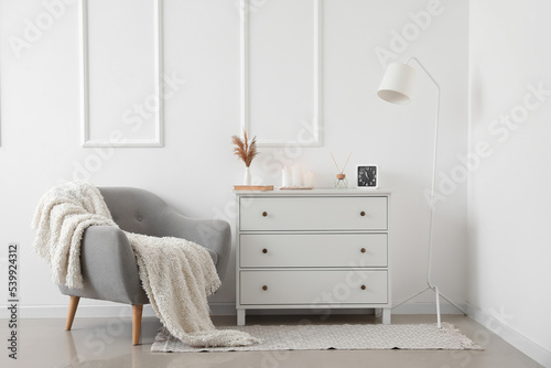 Interior of light living room with grey armchair  chest of drawers and lamp