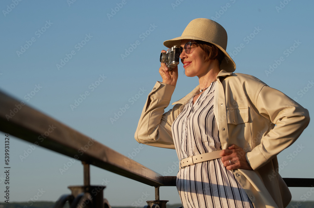 Obraz premium Woman tourist in a straw hat takes pictures on the street with a vintage camera