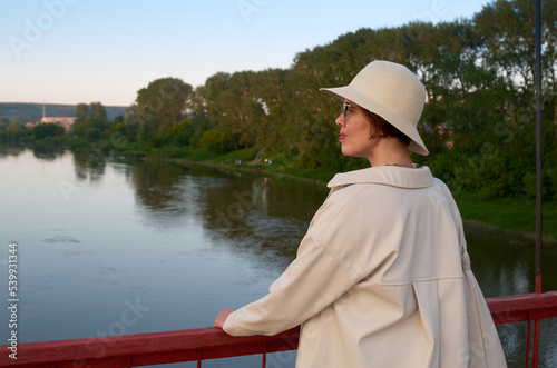 Portrait of travelling woman in hat on bridge against the backdrop of the evening river