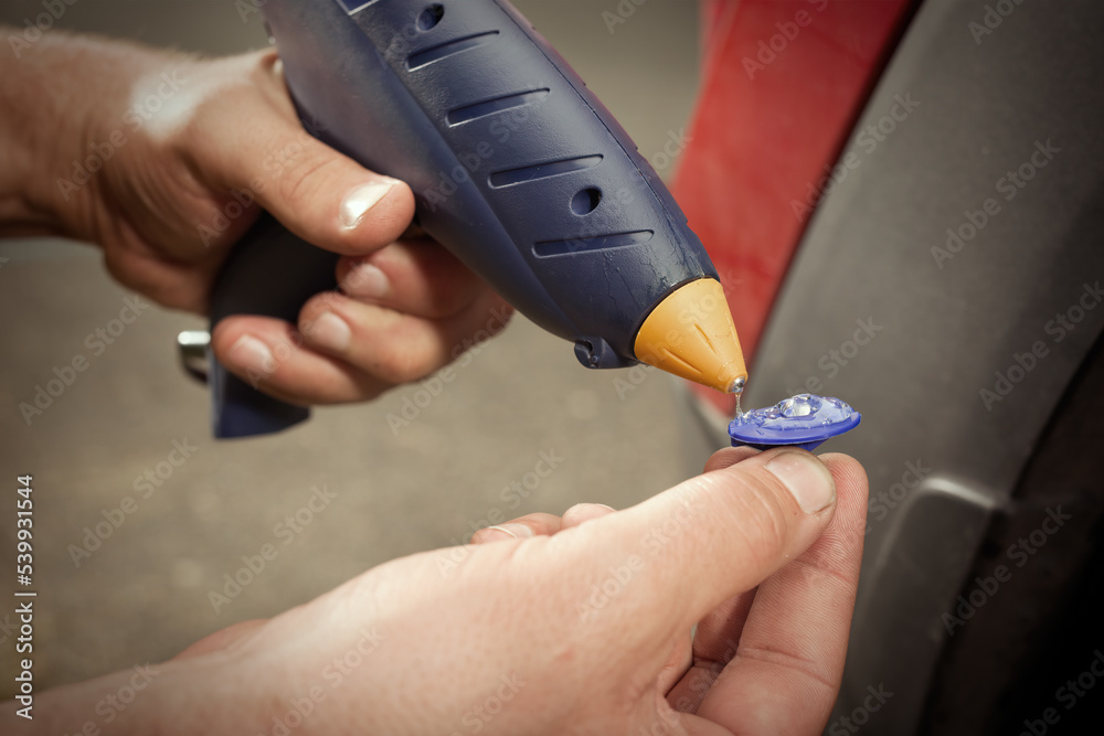 Fototapeta premium Car owner working on a dent repair with reverse hammer and glue