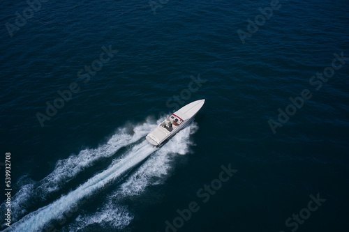 a man in a red hat on a speedboat fast movement on the water. White super speed big boat moves fast on dark water air view. © Berg